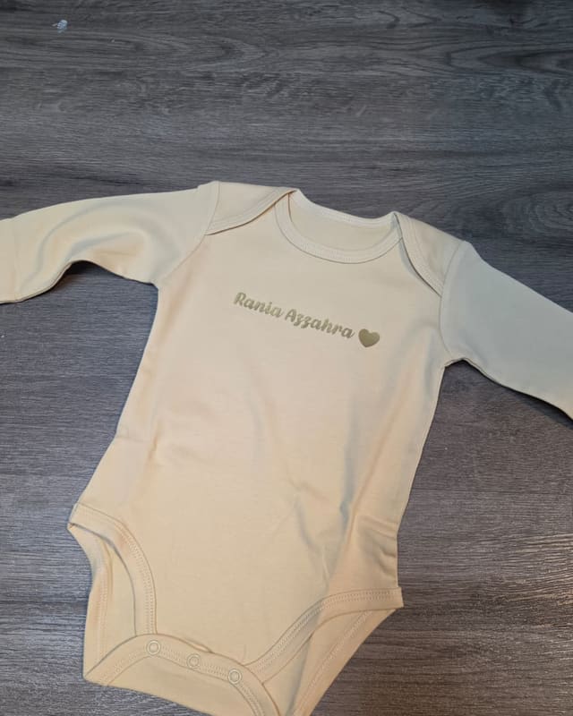 A cream long sleeve romper with a name printed in gold