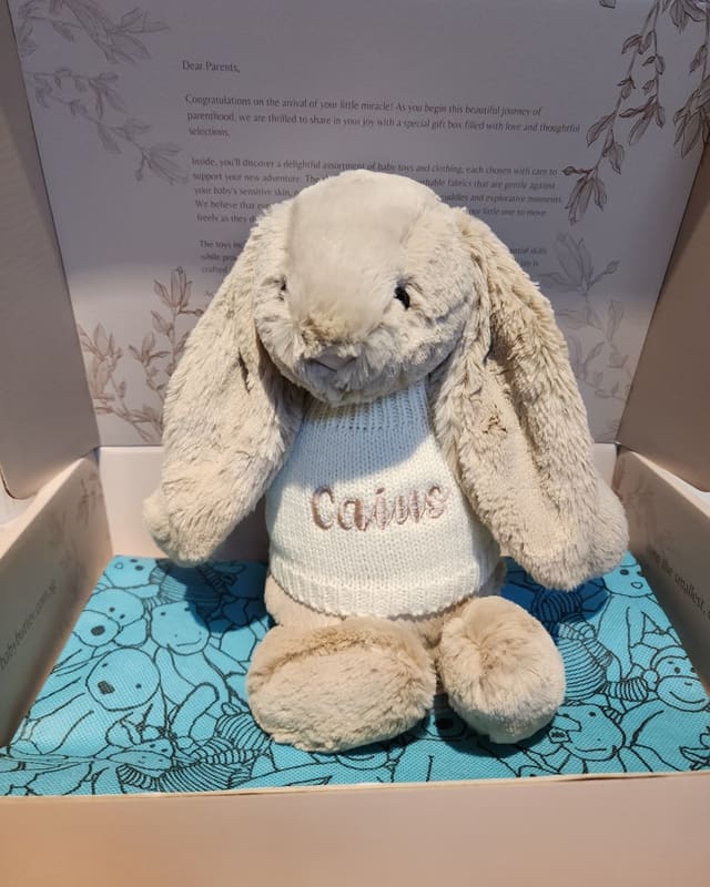 A Jellycat bunny in a knitted sweater embroidered with the name Caine